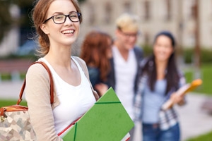 A woman in glasses holding a green folder and smiling at the camera